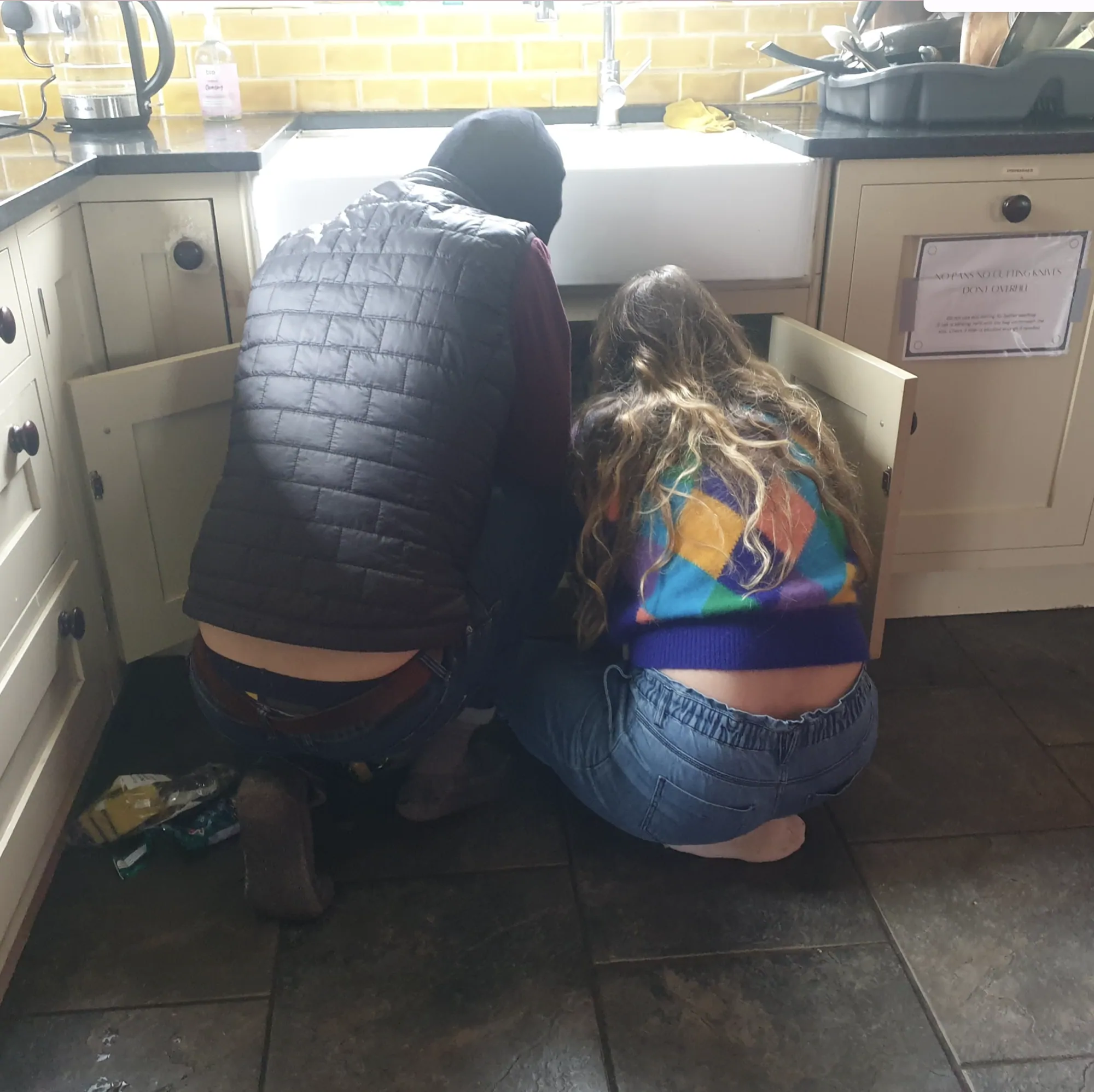 Two colivers crouched at the kitchen sink, fixing the plumbing together